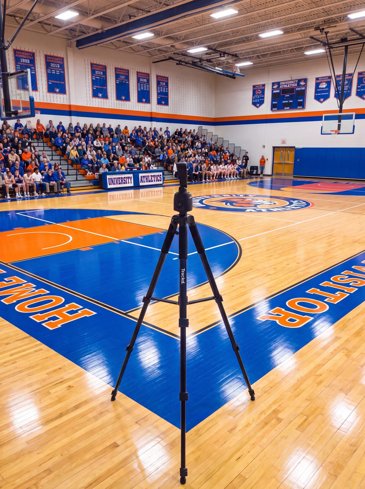 A Trackd tripod set up courtside at a packed high-school basketball game, facing a full crowd in the stands